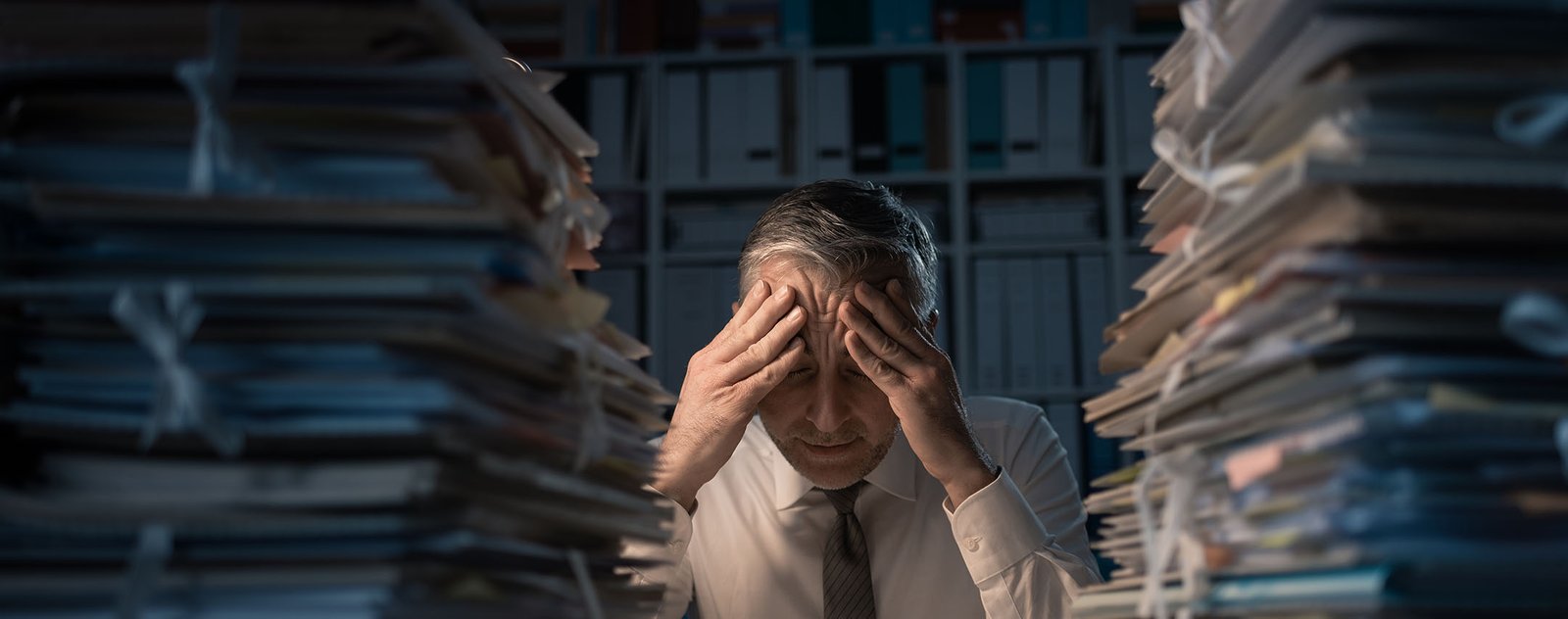 gentleman with his hands on his head sitting in front of two stacks of paper